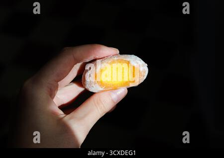 Nahaufnahme einer Frau, die gebissenes, gefrorenes gelbes Mochi-Eis mit Mangofüllung hält Stockfoto