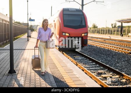 Schöne und elegante Geschäftsfrau, die mit Koffer am Bahnhof spaziert. Stockfoto
