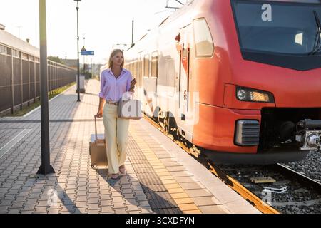 Schöne und elegante Geschäftsfrau, die mit Koffer am Bahnhof spaziert. Stockfoto
