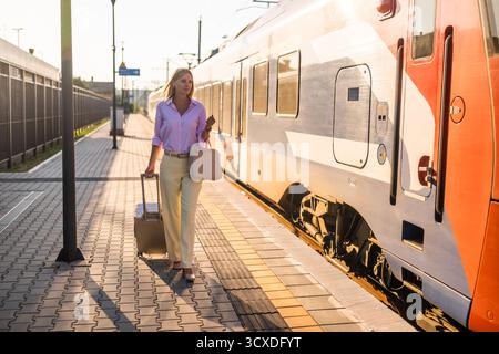 Schöne und elegante Geschäftsfrau, die mit Koffer am Bahnhof spaziert. Stockfoto