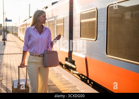 Schöne und elegante Geschäftsfrau, die mit Koffer am Bahnhof spaziert. Stockfoto