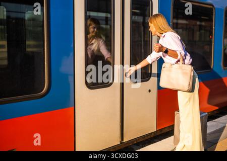 Elegante und selbstbewusste Geschäftsfrau, die am Bahnhof mit Koffer in einen Zug einsteigt. Stockfoto