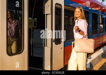 Elegante und selbstbewusste Geschäftsfrau, die am Bahnhof mit Koffer in einen Zug einsteigt. Stockfoto
