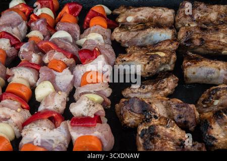 Rohe Schweinesieße und gegrillte Rippchen, die nebeneinander auf einem heißen Grill kochen, aus nächster Nähe Stockfoto