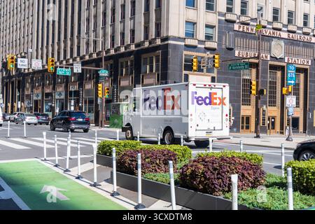 Ein Fedex-Truck fährt eine Stadtstraße entlang. Der Lkw ist weiß und hat das Fedex-Logo an der Seite. Die Straße ist voll mit Autos und Ampeln Stockfoto