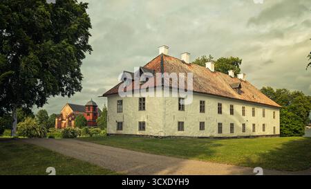 Blick auf das weiße Steinhaus und die rote mittelalterliche Skokloster-Kirche auf dem historischen Schlossgelände in Uppland, Schweden. Stockfoto