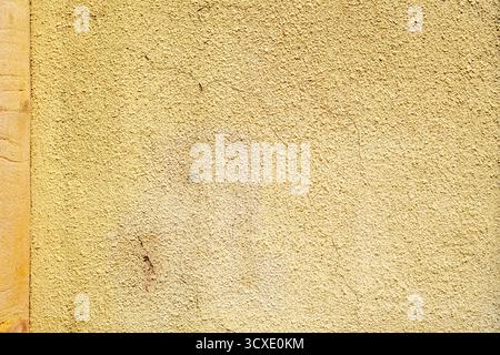 Alte, gelb lackierte raue Wand mit verwitterter, ungleichmäßiger Textur Stockfoto