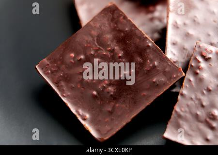 Nahaufnahme gebrochener dunkler bittersüßer Schokoladenstücke mit Beerenfüllung auf einer schwarzen Platte Stockfoto