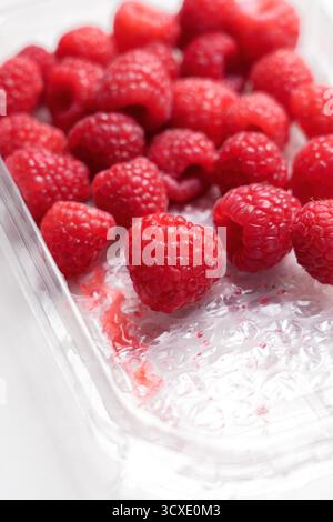 Himbeeren in offener Kunststoffverpackung auf weißer Oberfläche Stockfoto