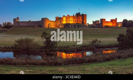 Ein Blick in der Abenddämmerung im frühen Herbst auf Alnwick Castle in Alnwick, Northumberland, von den Weiden aus mit Blick auf den Fluss ALN Stockfoto