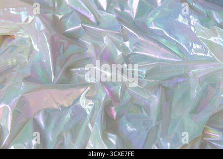 Glänzendes holografisches Material mit glatten Falten und schillernden Lichtreflexen. Abstrakter Hintergrund mit metallischer Textur und weichen Pastellfarben. Stockfoto