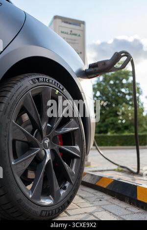 Ein Michelin-Reifen auf einem Tesla-Rad. Tesla Elektrofahrrad. Ein Tesla Elektroauto, das an einer Ladestation aufgeladen wird. Minsk, Weißrussland - 25. Juli 2022 Stockfoto