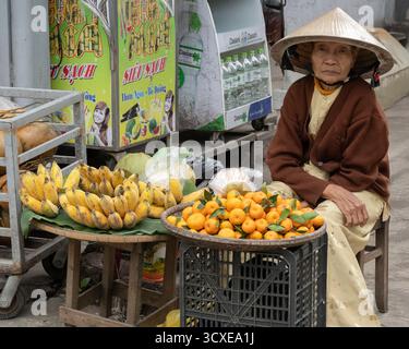 Ältere Frau, die Bananen und Orangen auf einem traditionellen Lebensmittelmarkt in Hue, Vietnam, verkauft Stockfoto