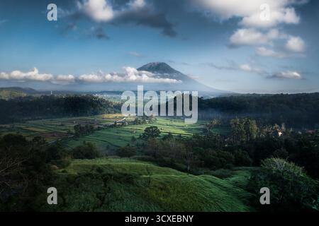 Majestätischer Blick auf den Vulkan Mount Agung auf Bali, der über nebeligen, üppigen Reisterrassen und einer grünen Landschaft ragt. Stockfoto