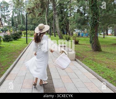Attraktive Frau in cremefarbenem, weißem Outfit, Strohhut im Park für einen Spaziergang Stockfoto