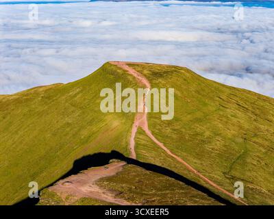 Wanderer gehen auf einem Pfad zu einem Berggipfel, der aus einem Wolkenmeer entspringt Stockfoto