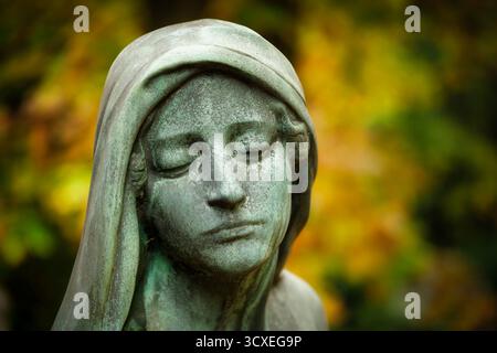 Eindrucksvolles Close-up Porträt Einer verwitterten Friedhofsstatue, sein melancholischer Ausdruck, eingerahmt von der weichen, strahlenden Unschärfe des goldenen Herbstlaub Stockfoto