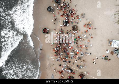 Blick aus der Vogelperspektive auf einen belebten Fischmarkt am Meer, wo sich Fischer, Boote und Einheimische an der tropischen Sandküste versammeln. Stockfoto