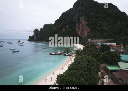Luftaufnahme der Tonsai Bay auf Koh Phi Phi Don mit Hauptpier, weißem Sandstrand, verankerten Longtail-Booten und hoch aufragenden Dschungel-bedeckten Klippen. Stockfoto
