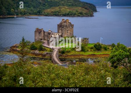 Eilean Donan Castle liegt auf einer üppigen Halbinsel mit Blick auf einen ruhigen See, mit fernen Bergen und lebhaftem Grün, die eine ruhige, historische Landschaft schaffen Stockfoto