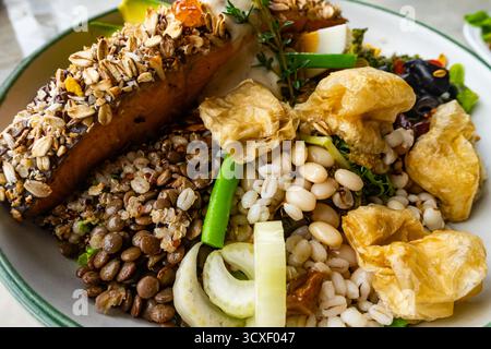 Hausgemachter köstlicher gemischter Müsli-Salat mit Avocado, grünem Gemüse, Oliven- und gebratenem Lachssteak auf weißer Keramikplatte auf dem Esstisch. Stockfoto
