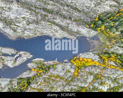 Direkte Aufnahme eines schmalen Kanals aus dunklem Wasser, flankiert von exponiertem, gebrochenem grauen Felsen und farbenfrohem Herbstwald, mit einem kleinen Boot sichtbar i Stockfoto