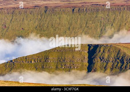 Zwei Wanderer stehen in der Abenddämmerung auf einem Berggipfel über einem Wolkenmeer in Wales Stockfoto