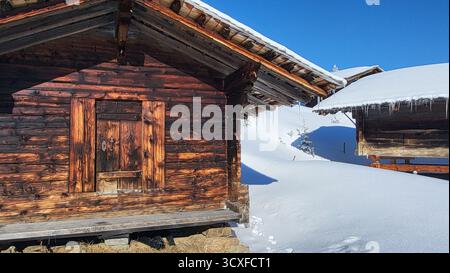 Eine wunderschöne Winterszene in den Schweizer Alpen mit einer typischen hölzernen Almhütte umgeben von tiefem Schnee unter einem klaren, tiefblauen Himmel, Schweiz Stockfoto