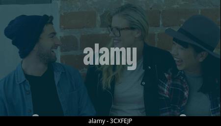 Lachende Freunde tragen ein Denim-Hemd, Strickmütze und einen Hut mit breiter Krempe, die auf einer Bank im Ziegelloft plaudern Stockfoto