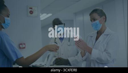 Bietet maskierte Krankenschwester in Peelings an, die Desinfektionsspray an maskierten Arzt am Krankenhausschreibtisch weitergeben Stockfoto