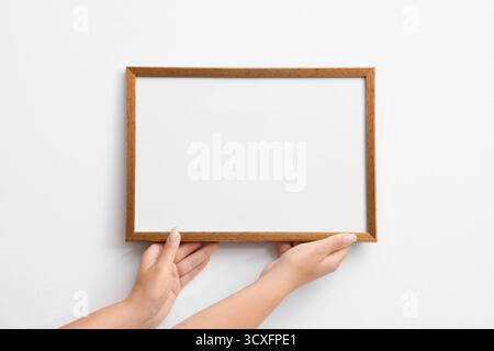 Frau, die einen leeren Diplomrahmen an der weißen Wand hängt, Großaufnahme. Modell für Design Stockfoto