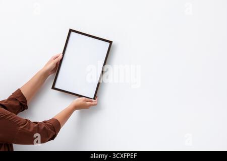 Frau, die einen leeren Diplomrahmen an der weißen Wand hängt, Großaufnahme. Modell für Design Stockfoto