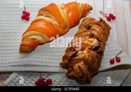 Zwei köstliche Croissants auf einem hellen Küchentuch mit roten Viburnum-Beeren auf Holztisch. Konzept von hausgemachtem Gebäck, Frühstück und gemütlichem Mo Stockfoto