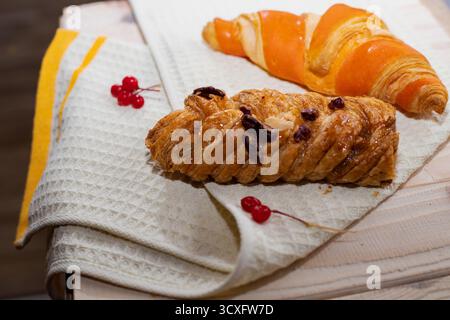 Zwei köstliche Croissants auf einem hellen Küchentuch mit roten Viburnum-Beeren auf Holztisch. Konzept von hausgemachtem Gebäck, Frühstück und gemütlichem Mo Stockfoto