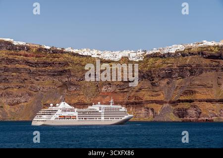 Panoramablick auf die Stadt Fira in Santorin, Griechenland, vom Meer aus gesehen, mit traditionellen weißen Gebäuden auf den Caldera-Klippen und einem großen Kreuzfahrtschiff Stockfoto
