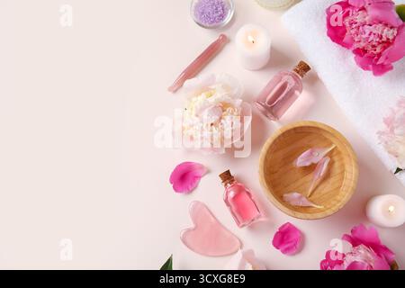 Flaschen mit ätherischem Öl mit Kerzen, Meersalz, guasha-Massagewerkzeug und schönen Pfingstrosenblüten auf beigem Hintergrund Stockfoto