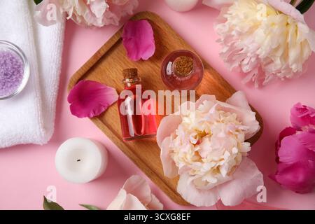 Holztablett mit Flaschen ätherischen Öls, Kerze und schönen Pfingstrosenblüten auf rosa Hintergrund Stockfoto