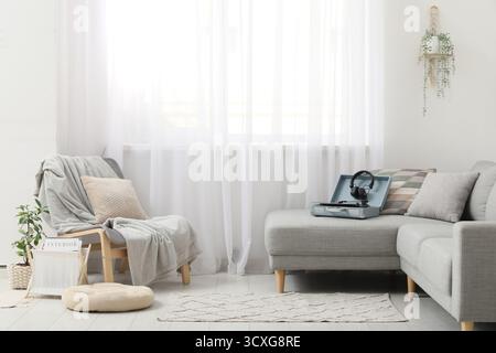 Stilvolles Wohnzimmer mit Sessel, Plattenspieler und Kopfhörern auf grauem Sofa Stockfoto