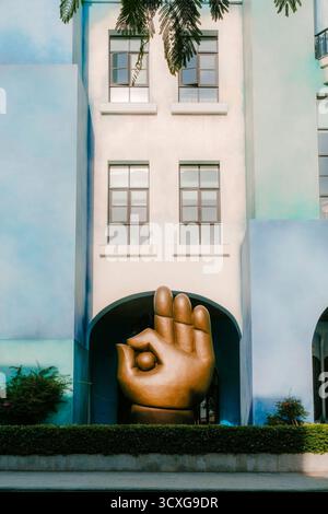 Moderne architektonische Fassade mit einer großen goldenen Handskulptur, die eine „OK“-Geste darstellt, eingerahmt von sanften blauen und weißen Wänden Stockfoto