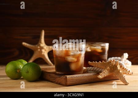 Tablett mit Gläsern kalten Cuba Libre Cocktails, Seesternen und Seil auf hölzernem Hintergrund Stockfoto
