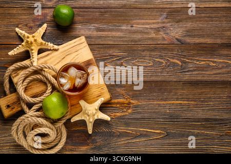 Bord mit einem Glas kalten Cuba Libre Cocktail, Sternenfischen und Seil auf hölzernem Hintergrund Stockfoto