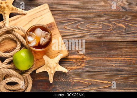 Bord mit einem Glas kalten Cuba Libre Cocktail, Sternenfischen und Seil auf hölzernem Hintergrund Stockfoto
