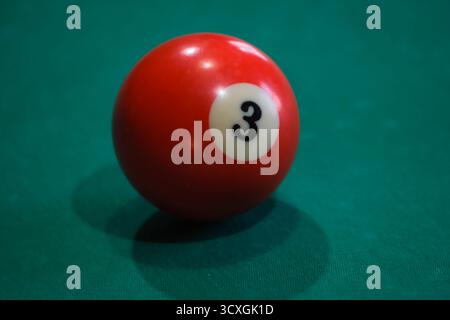 Rote 8-Kugel auf grünem Billardtisch unter sanftem Licht, Symbol für Fokus und Entscheidung im Billard- oder Spielstrategiekonzept Stockfoto