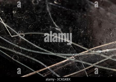Zerbrochenes nasses Glas liegt auf einer schwarzen Platte mit einer ungleichmäßigen Textur, Stücke von durchsichtigem Glas, das in der Konstruktion verwendet wird, bedeckt mit Wassertröpfchen Stockfoto