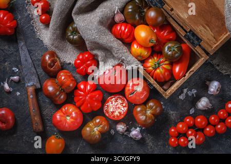 Viele verschiedene Arten, Formen und Größen von Tomaten in einer alten Holzkiste und auf einer dunklen Oberfläche, flach liegend, Draufsicht. Erntekonzept Stockfoto