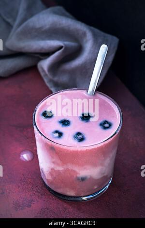 Hochwertige Heidelbeeren und ein Heidelbeeren-Smoothie mit Mandelmilch auf einem Teakholztisch im Freien Stockfoto