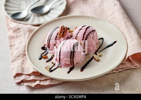 Rosafarbenes Himbeereis mit Schokoladensauce und Nüssen auf Teller Stockfoto