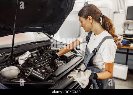 Eine erfahrene Mechanikerin arbeitet an einem Automotor und zeigt ihr Fachwissen und ihre technischen Fähigkeiten Stockfoto