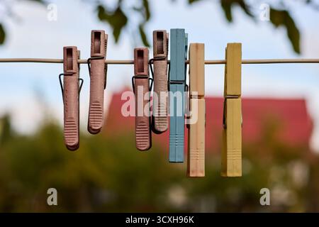 Nahaufnahme von farbenfrohen, Vintage-Plastik-Kleiderschalen, die an einem Draht vor einem verschwommenen Hintergrund von Bäumen und einem Gebäude mit rotem Dach hängen. Stockfoto