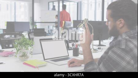 Verstellbare Lampe, männlich in kariertem Hemd, sitzt am Schreibtisch mit offenem Laptop, Terrarium, Kopierraum Stockfoto